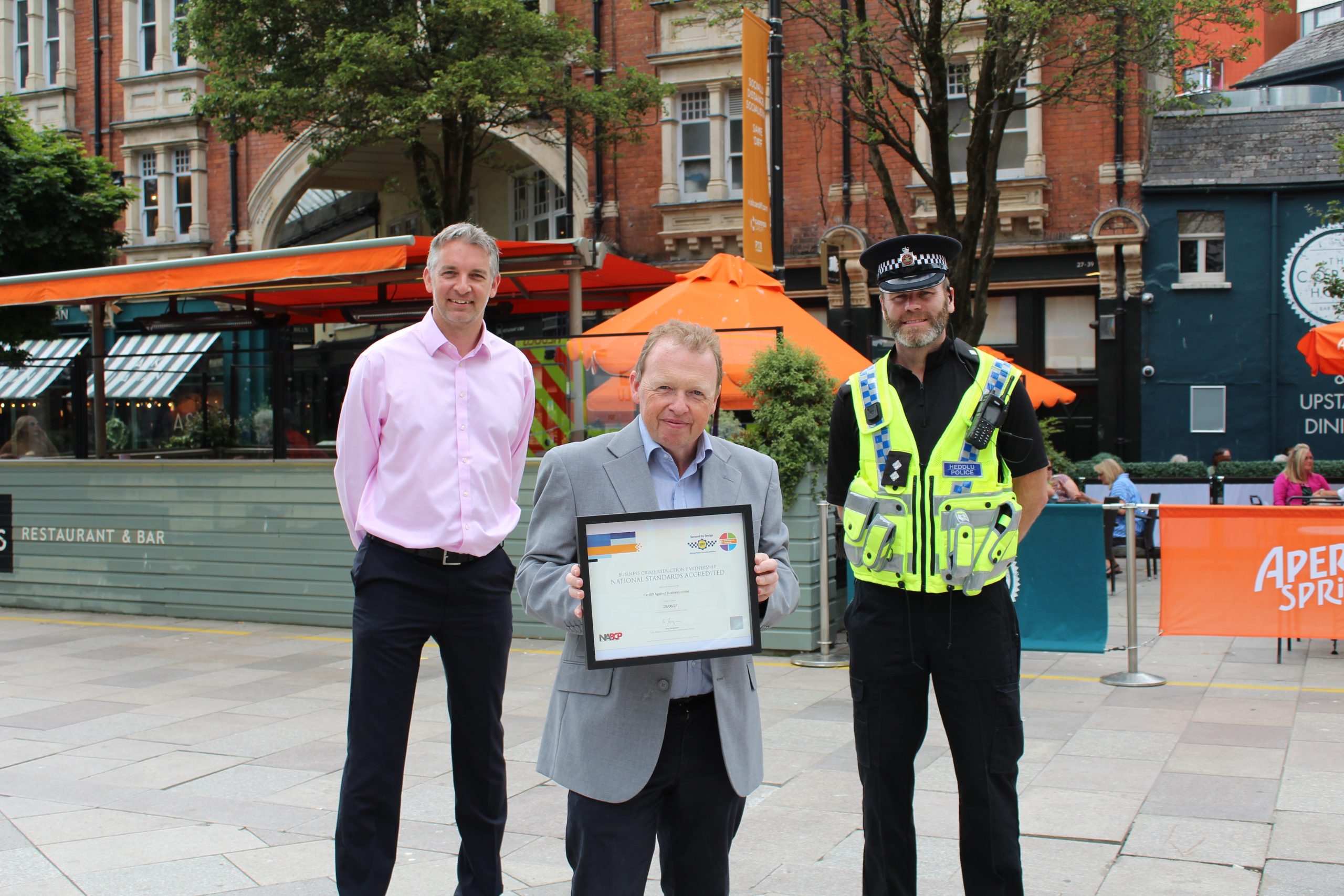 three men standing in Cardiff city centre with one man holding the reaccreditation certificate